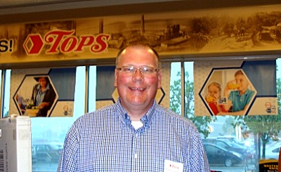 Store Manager Rich Szachta standing in front of the new mural in the Tops vestibule, featuring scenes from Lansing history.